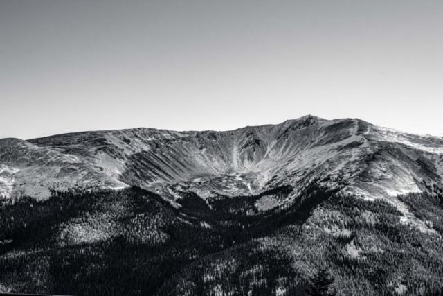 large crater sits in the center of forested mountains; black and white