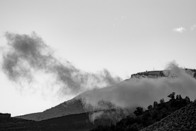 smoke billows up from the hilly landscape; black and white